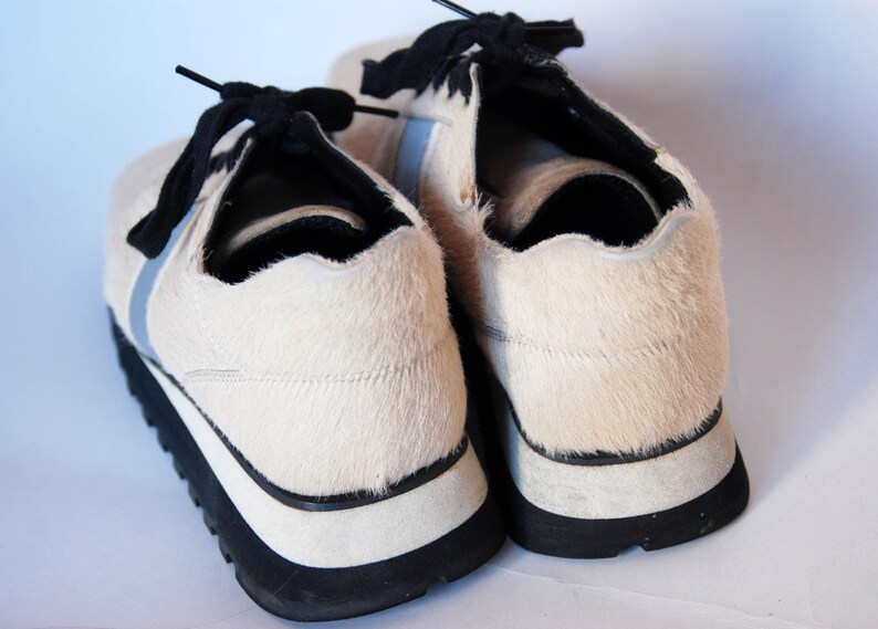 May include: A pair of white furry trainers with black laces and a black and white sole.