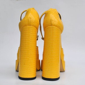 May include: A pair of yellow platform sandals with a crocodile-embossed texture. The sandals have a thick, chunky heel and an ankle strap.