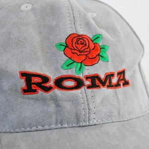 May include: Gray baseball cap with a red rose and the word "ROMA" embroidered in black.