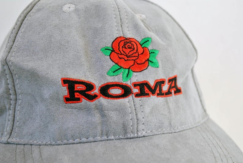 May include: Gray baseball cap with a red rose and the word "ROMA" embroidered in black.