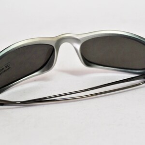 May include: Silver and gray sunglasses with a black metal frame and gray lenses. The sunglasses have the text "ICE 004 YU" printed on the inside of the right lens.