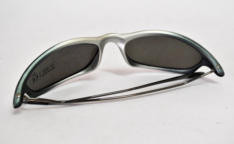 May include: Silver and gray sunglasses with a black metal frame and gray lenses. The sunglasses have the text "ICE 004 YU" printed on the inside of the right lens.