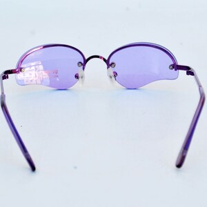 May include: Purple rimless sunglasses with oval lenses and a thin metal frame. The lenses are a light purple colour, and the frame is a darker purple. The sunglasses have a modern, minimalist design.