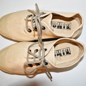 May include: A pair of off-white canvas sneakers with grey laces. The inside of the shoes has the word "BIG" printed in black.