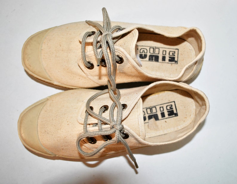 May include: A pair of off-white canvas sneakers with grey laces. The inside of the shoes has the word "BIG" printed in black.