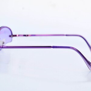 May include: A pair of purple-tinted, round-lens spectacles with a slender, metallic frame. The glasses feature a minimalist design, with a bridge and temples in a matching purple shade. The lenses are a solid purple colour, and the overall aesthetic is sleek and modern.
