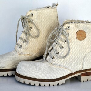 May include: A pair of white canvas high-top boots with brown laces and a brown leather patch on the side.