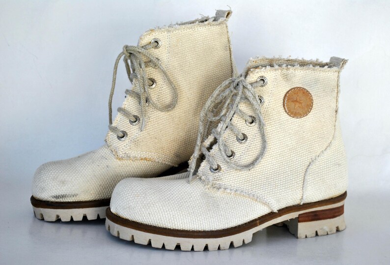 May include: A pair of white canvas high-top boots with brown laces and a brown leather patch on the side.