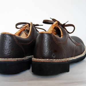 K&ouml;nnte beinhalten: Ein Paar braune Lederschn&uuml;rschuhe mit strukturierter Oberfl&auml;che. Die Schuhe haben eine dicke schwarze Sohle und eine wei&szlig;e Nahtdetail entlang der Kante.