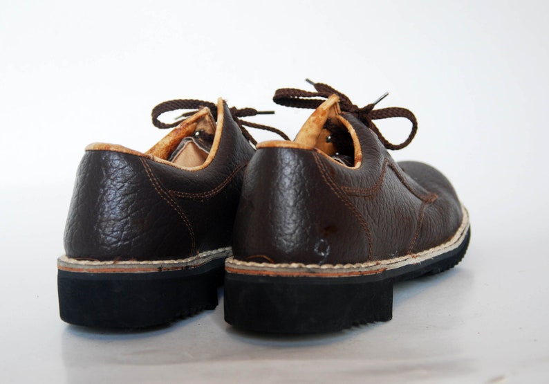 K&ouml;nnte beinhalten: Ein Paar braune Lederschn&uuml;rschuhe mit strukturierter Oberfl&auml;che. Die Schuhe haben eine dicke schwarze Sohle und eine wei&szlig;e Nahtdetail entlang der Kante.