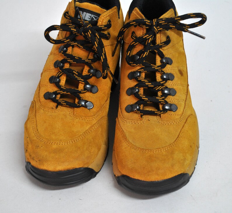 May include: A pair of yellow suede hiking boots with black laces. The boots have a black rubber sole.