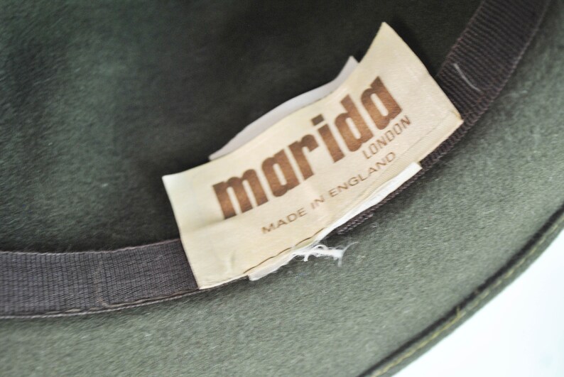 May include: A green felt fedora hat with a brown ribbon and a white label that reads "marida LONDON MADE IN ENGLAND".
