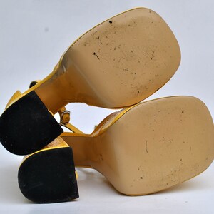 May include: A pair of yellow platform sandals with black soles. The sandals have a strap across the ankle and a buckle fastening.
