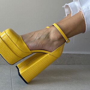 May include: Yellow platform heels with a crocodile-embossed leather upper and a thick platform sole.