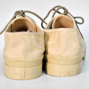May include: A pair of off-white canvas sneakers with light grey laces. The shoes have a thick rubber sole and are untied.