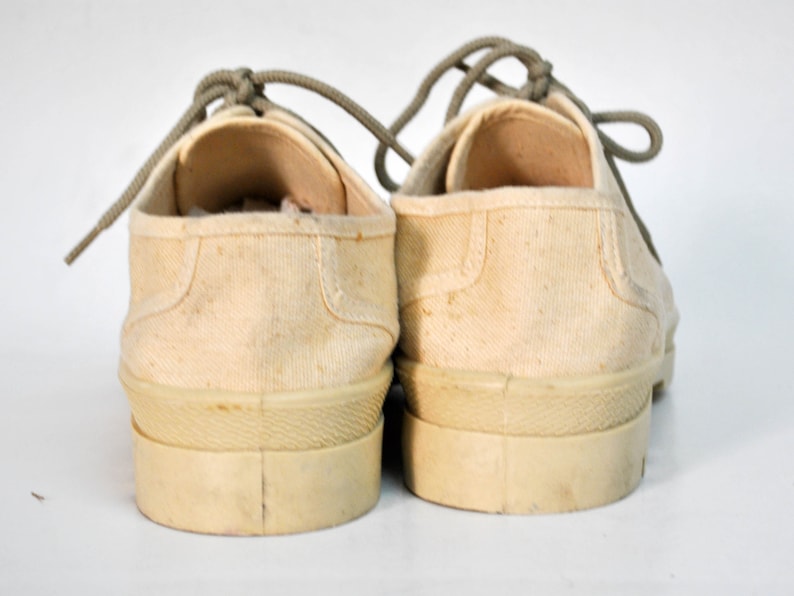 May include: A pair of off-white canvas sneakers with light grey laces. The shoes have a thick rubber sole and are untied.