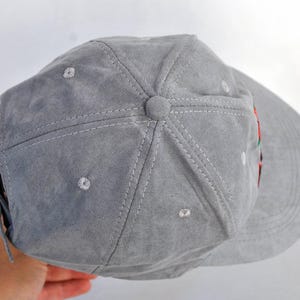 May include: A gray suede baseball cap with a black brim. The cap has a stitched design and a small button on the top.