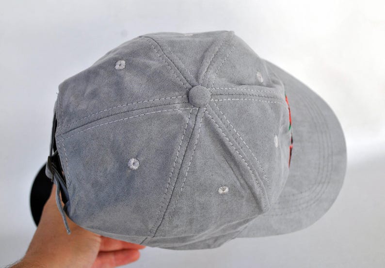 May include: A gray suede baseball cap with a black brim. The cap has a stitched design and a small button on the top.