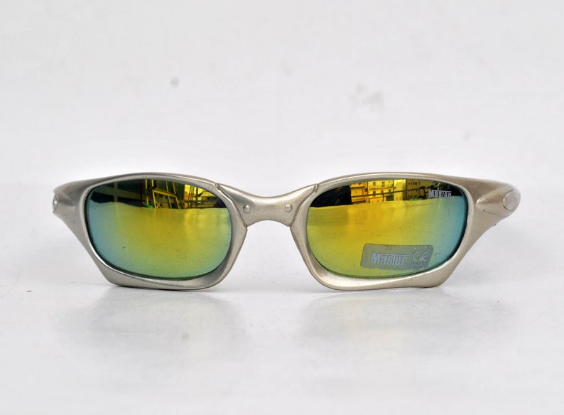 May include: Silver-toned sunglasses with a gold mirrored lens. The sunglasses have a Master CE label on the right lens.