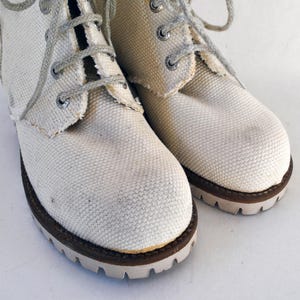 May include: A pair of white canvas high-top boots with brown laces and brown soles.