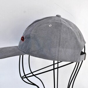 May include: A gray suede baseball cap with red embroidered text on the front.
