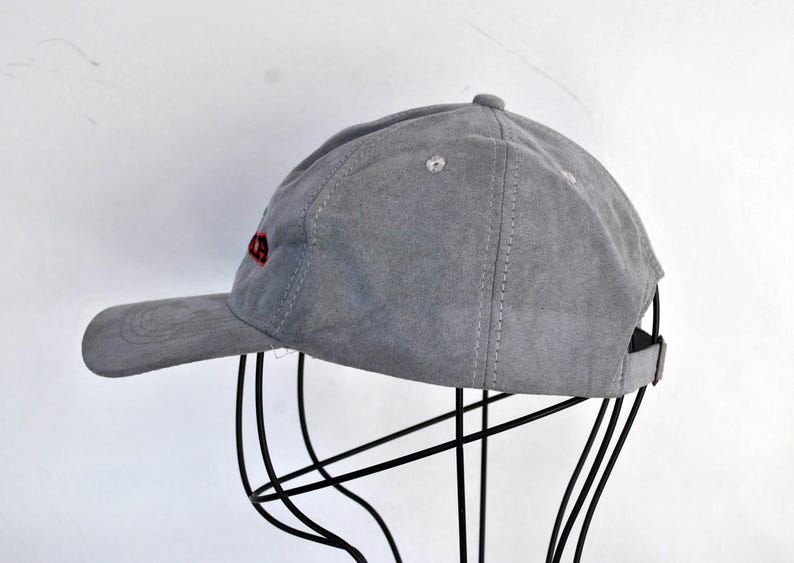 May include: A gray suede baseball cap with red embroidered text on the front.