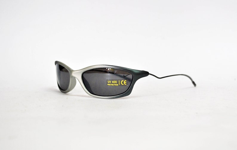 May include: Gray and black sunglasses with a thin black frame and gray lenses. The sunglasses have "UV 400 PROTECTION CE" printed on the right lens.