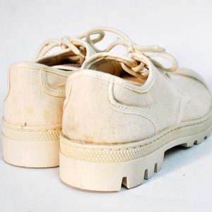 May include: A pair of off-white canvas shoes with thick white soles and laces. The shoes are worn and have a vintage look.