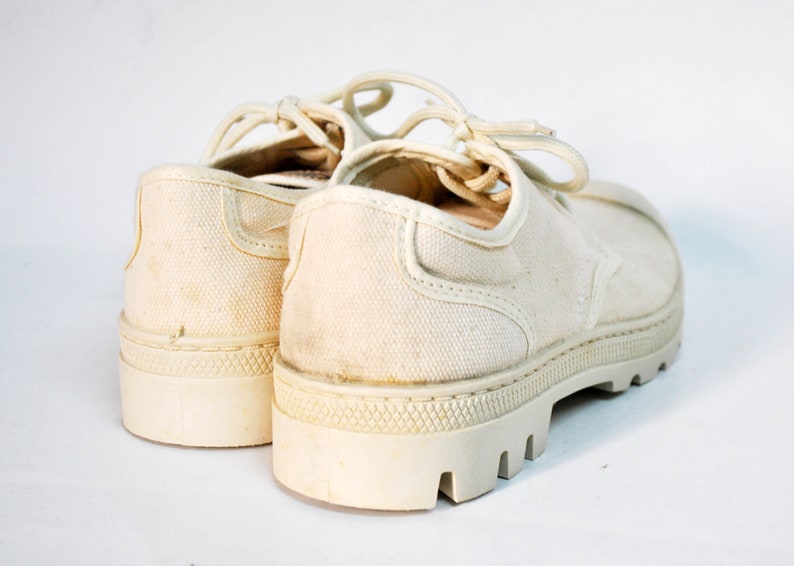 May include: A pair of off-white canvas shoes with thick white soles and laces. The shoes are worn and have a vintage look.