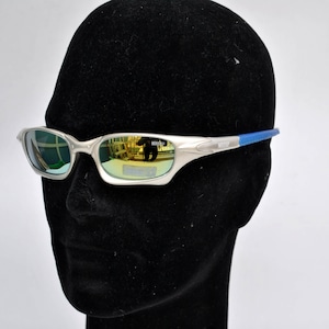 May include: Silver-toned sunglasses with blue accents and mirrored lenses. The lenses reflect a green and gold color.