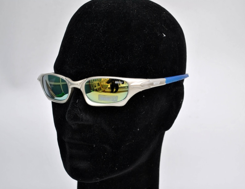 May include: Silver-toned sunglasses with blue accents and mirrored lenses. The lenses reflect a green and gold color.