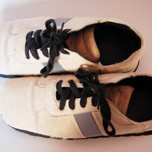May include: A pair of white leather trainers with black laces and a grey stripe on each shoe.