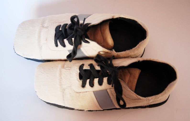 May include: A pair of white leather trainers with black laces and a grey stripe on each shoe.