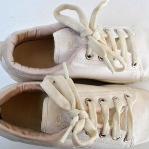 K&ouml;nnte beinhalten: Ein Paar wei&szlig;e Canvas-Sneaker mit wei&szlig;en Schn&uuml;rsenkeln. Die Schn&uuml;rsenkel sind oben auf den Schuhen zu einer Schleife gebunden.