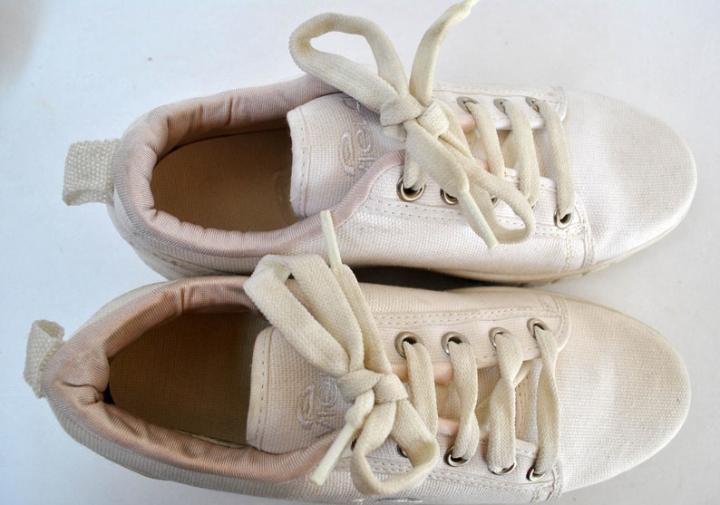 K&ouml;nnte beinhalten: Ein Paar wei&szlig;e Canvas-Sneaker mit wei&szlig;en Schn&uuml;rsenkeln. Die Schn&uuml;rsenkel sind oben auf den Schuhen zu einer Schleife gebunden.