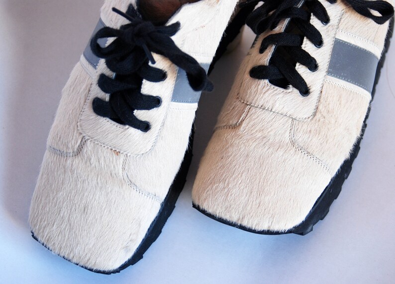 May include: A pair of white furry trainers with black laces and a silver reflective stripe on each side.