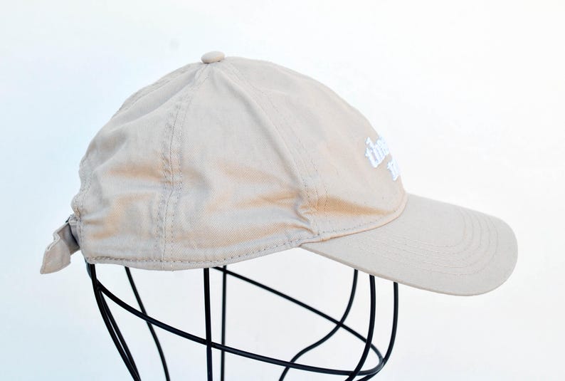 May include: A beige baseball cap with a white embroidered logo that says "The Daily Grind".
