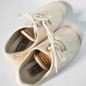 May include: A pair of off-white canvas sneakers with brown leather labels that read "doctor P. by proprio".