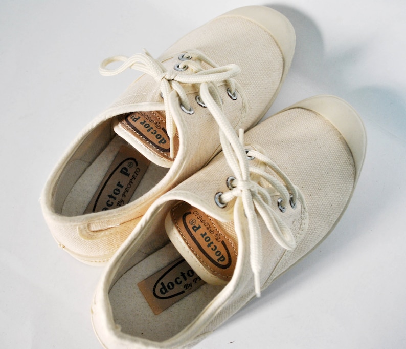 May include: A pair of off-white canvas sneakers with brown leather labels that read "doctor P. by proprio".