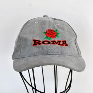 May include: A gray suede baseball cap with a red rose and the word "ROMA" embroidered in black and red.
