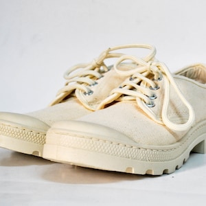 May include: A pair of off-white canvas low-top shoes with white laces and a thick white rubber sole.