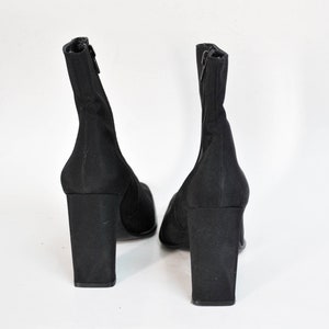 May include: A pair of black ankle boots with a block heel. The boots are made of a stretchy fabric and have a zipper on the back.