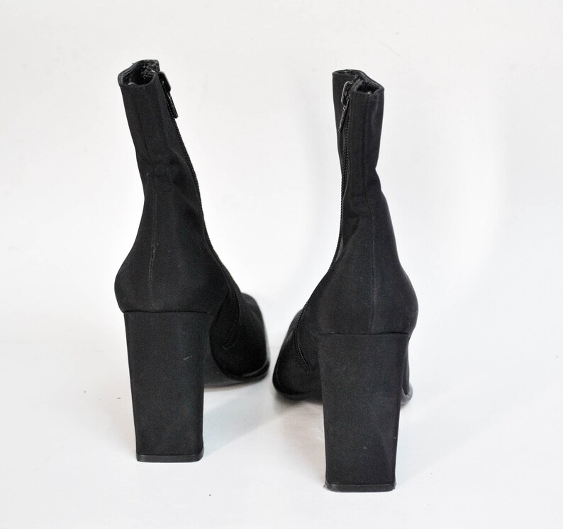 May include: A pair of black ankle boots with a block heel. The boots are made of a stretchy fabric and have a zipper on the back.