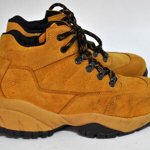 May include: Tan suede hiking boots with black laces and a black "NEXUS" logo on the side. The boots have a thick, rugged sole.