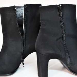 May include: A pair of black suede ankle boots with a pointed toe and a block heel. The boots have a zipper on the inside of each boot.