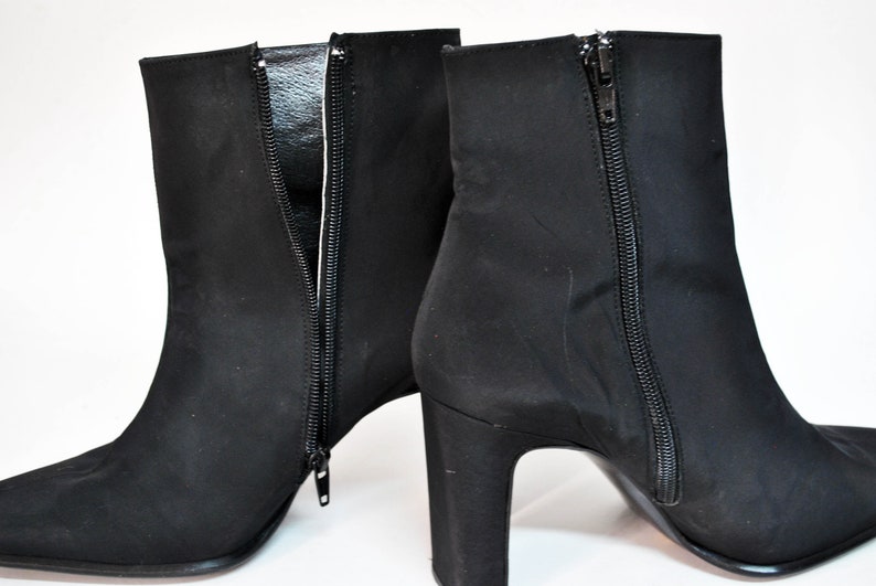 May include: A pair of black suede ankle boots with a pointed toe and a block heel. The boots have a zipper on the inside of each boot.