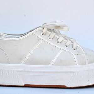 May include: White platform sneakers with a lace-up closure. The shoes have a thick white sole and a slightly distressed look.