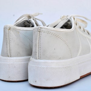 May include: A pair of white leather sneakers with white laces. The sneakers have a white rubber sole with a textured pattern.