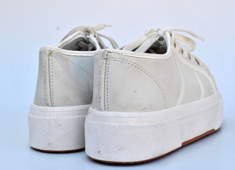 May include: A pair of white leather sneakers with white laces. The sneakers have a white rubber sole with a textured pattern.