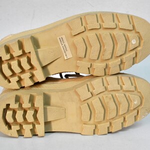 May include: Close-up of the soles of a pair of tan canvas boots. The boots have a textured rubber sole and the text "DESIGN TEXTILE SEMELLE SYNTHETIQUE" is printed on the sole of one boot.